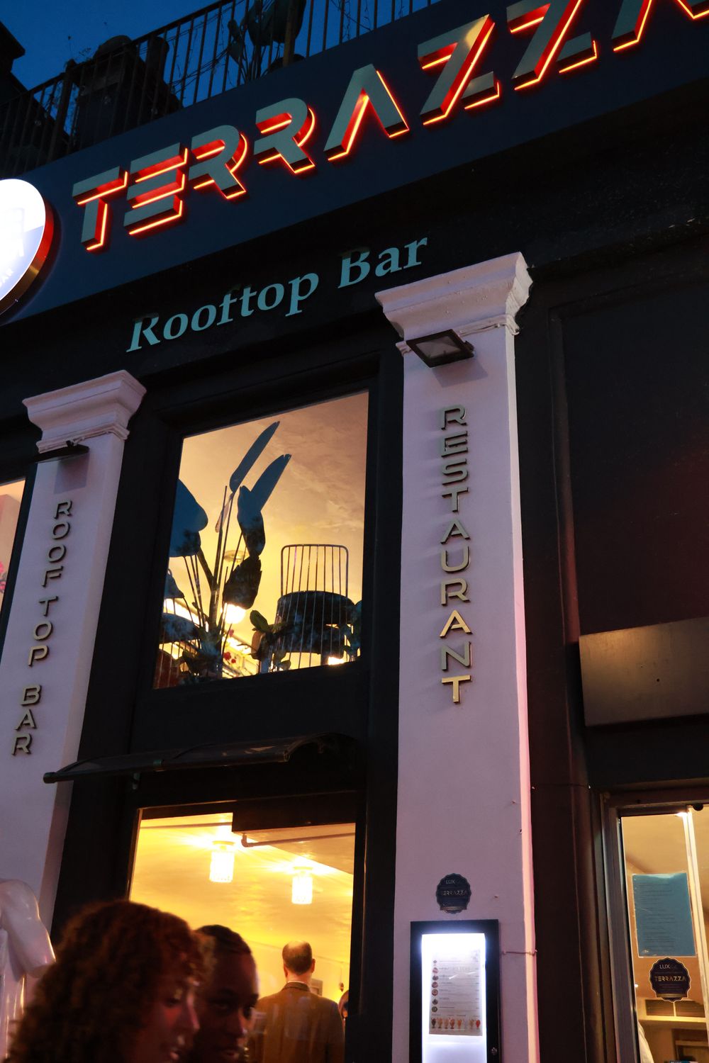 Terrazza lit up at dusk on Haverstock Hill, with its red sign and statue at the door
