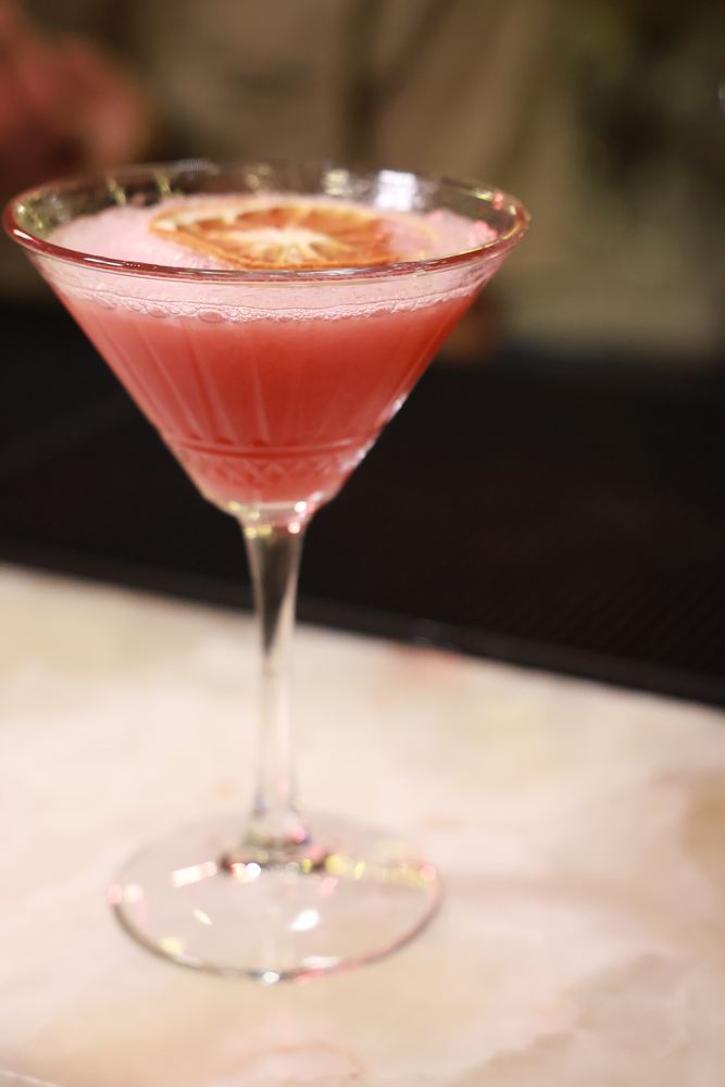 A pink cocktail with a dried orange slice on the marble bar