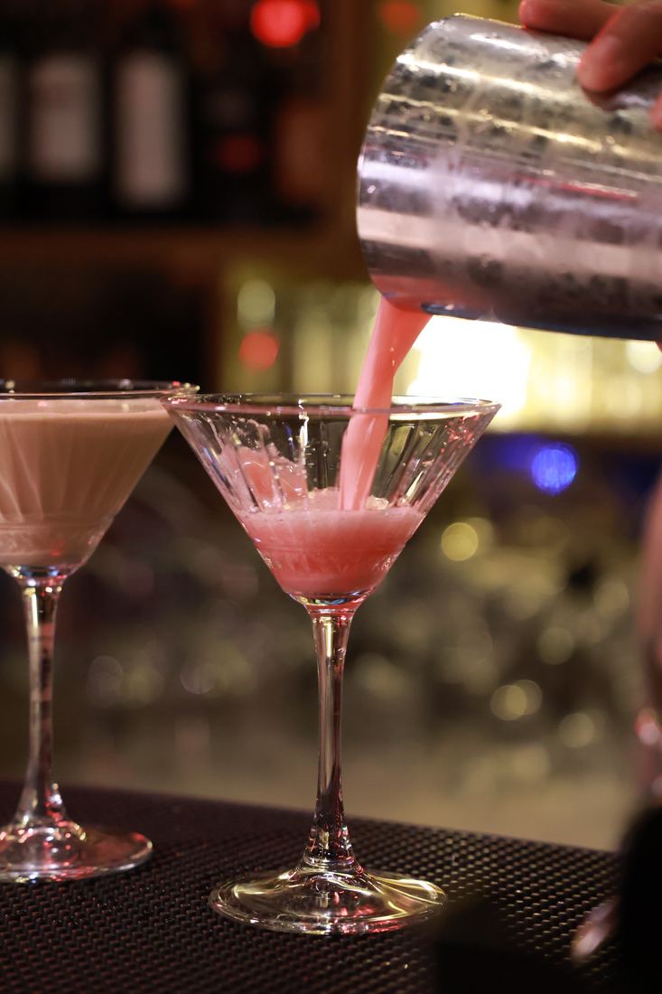 A pink cocktail being poured into a martini glass